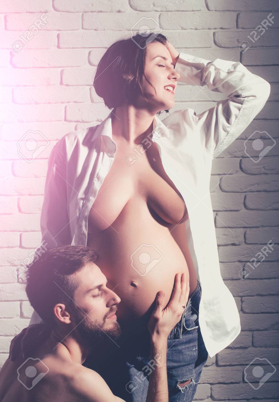お母さんの家族ヌードの画像 かなり満足しているセクシーな女性またはかわいい妊娠中の女の子の裸の家族親カップル  ラウンド腹や白いシャツとレンガ壁の背景にハンサムなひげを生やした男のヒップスターの腹部の母の日の写真素材・画像素材 Image 71824797