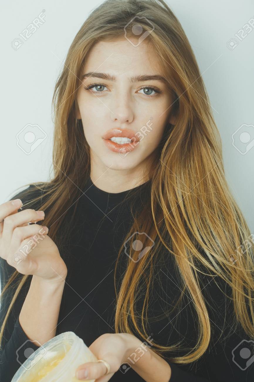 Hübsches Mädchen oder schöne Frau mit jungen Gesicht Haut und lange, blonden Haaren, ein Gel oder Balsam auf sexye Lippen aus Glas auf weiße Wand Hübsches Mädchen oder schöne Frau mit jungen Gesicht Haut und lange, blonden Haaren, ein Gel oder Balsam auf sexye Lippen aus Glas auf weiße Wand