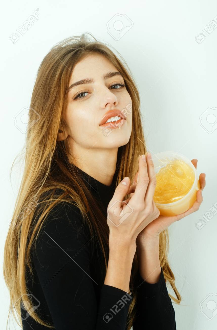 Hübsches Mädchen oder schöne Frau mit jungen Gesicht Haut und lange, blonden Haaren, ein Gel oder Balsam auf sexye Lippen aus Glas auf weiße Wand Hübsches Mädchen oder schöne Frau mit jungen Gesicht Haut und lange, blonden Haaren, ein Gel oder Balsam auf sexye Lippen aus Glas auf weiße Wand
