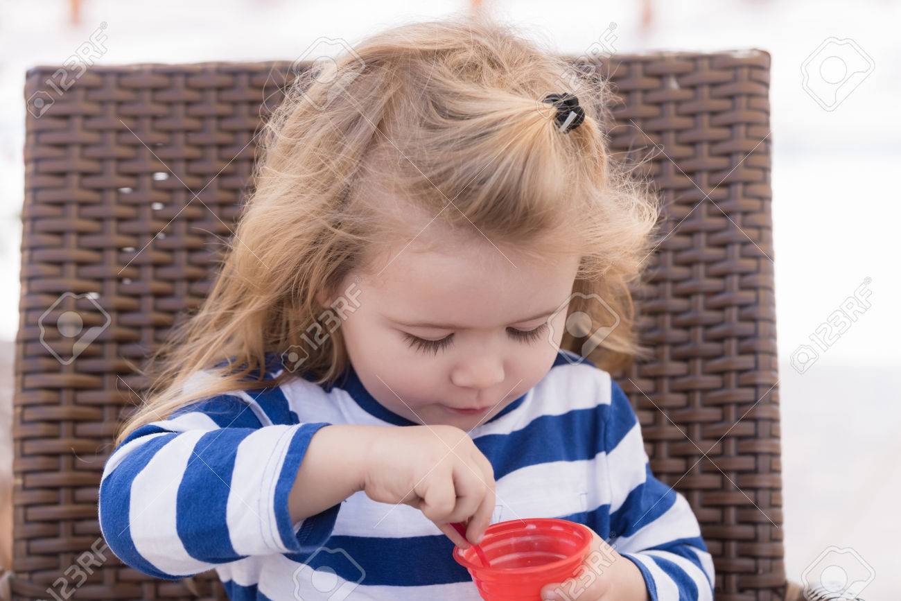 Bebe Garcon Mignon Petit Petit Enfant Avec De Longs Cheveux Blonds Dans Des Vetements Bleu Raye Manger De La Creme Glacee Savoureuse Dessert Rose Congele Dans La Tasse Sur Une Chaise Dans