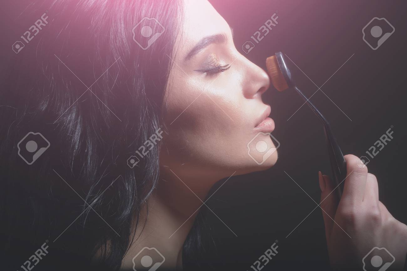 ファッショナブルなモデル ブルネットの髪を持つかわいいセクシーな女の子は長いまつげ 愛らしい顔にファッショナブルなアイメイクが基礎メイク顔近くにブラシを保持します 美容と化粧品 の写真素材 画像素材 Image