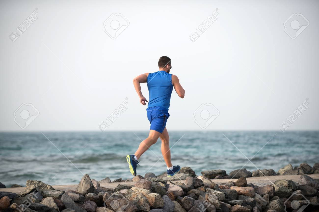 Back view running male athlete boy in blue sportswear with muscular strong body on stone coast of ocean in summer on background of sky and water - 81543244 Back view running male athlete boy in blue sportswear with muscular strong body on stone coast of ocean in summer on background of sky and water - 81543244