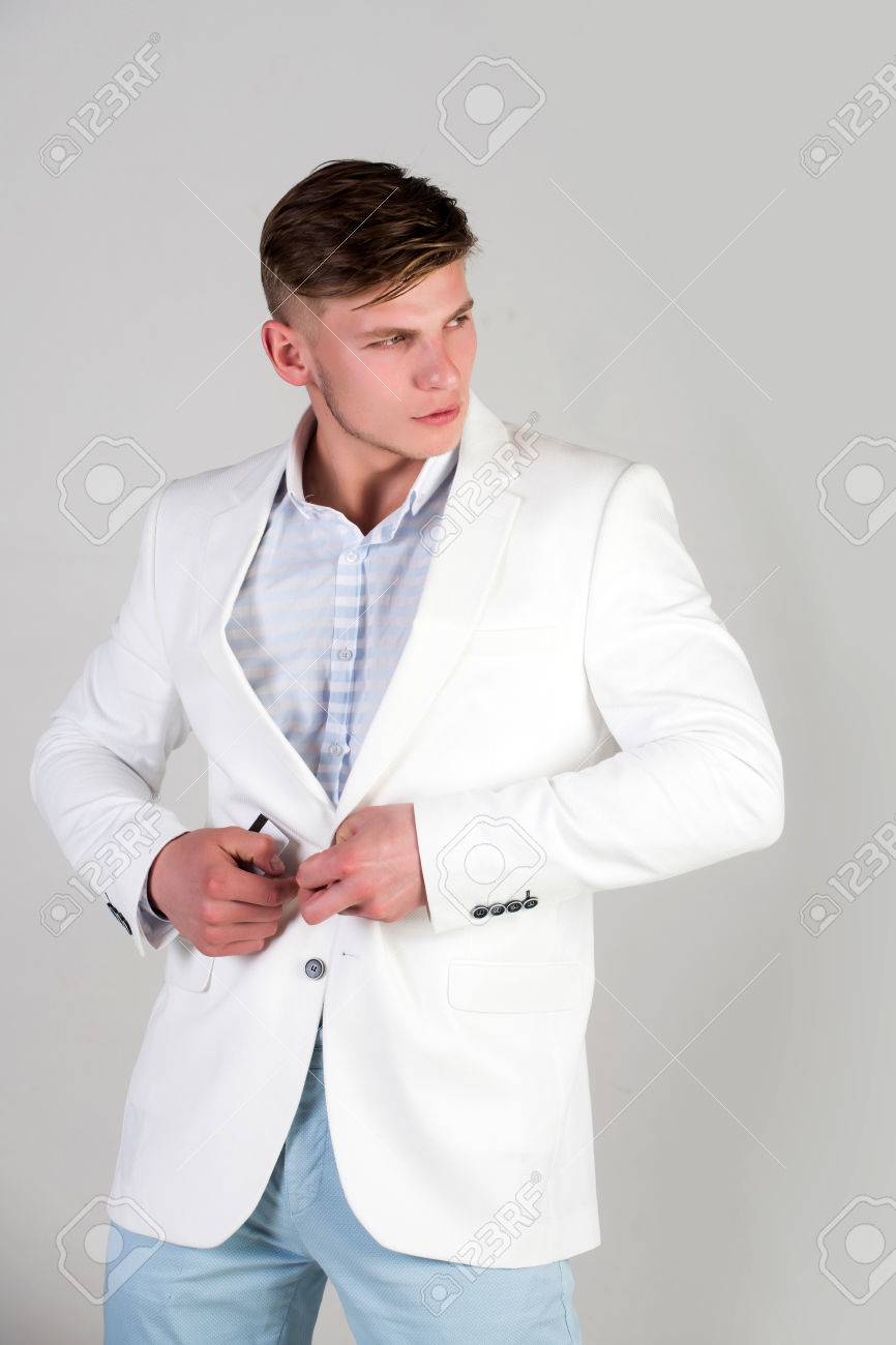 Macho Abotonándose La Chaqueta Blanca. Hombre Vistiendo Camisa A Rayas Y Pantalones Azules. Modelo Posando En Traje Casual Sobre Fondo Gris. Concepto De Moda Fotos, Retratos, Imágenes Y Fotografía De Archivo Libres