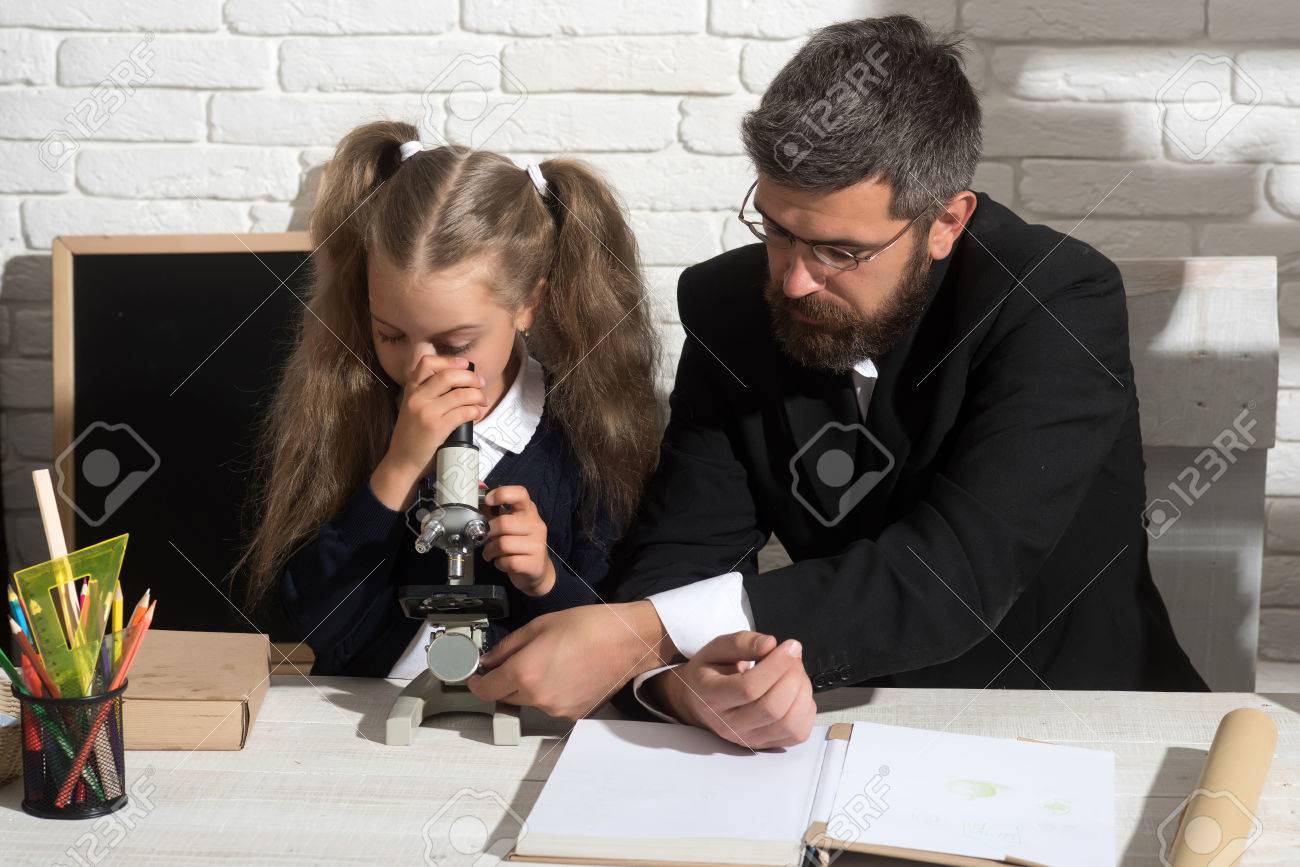 Girl And Man Sit By Desk And Looks Into Microscope Teacher And Schoolgirl In Study Girl And Man Sit By Desk And Looks Into Microscope Teacher And Schoolgirl In Study