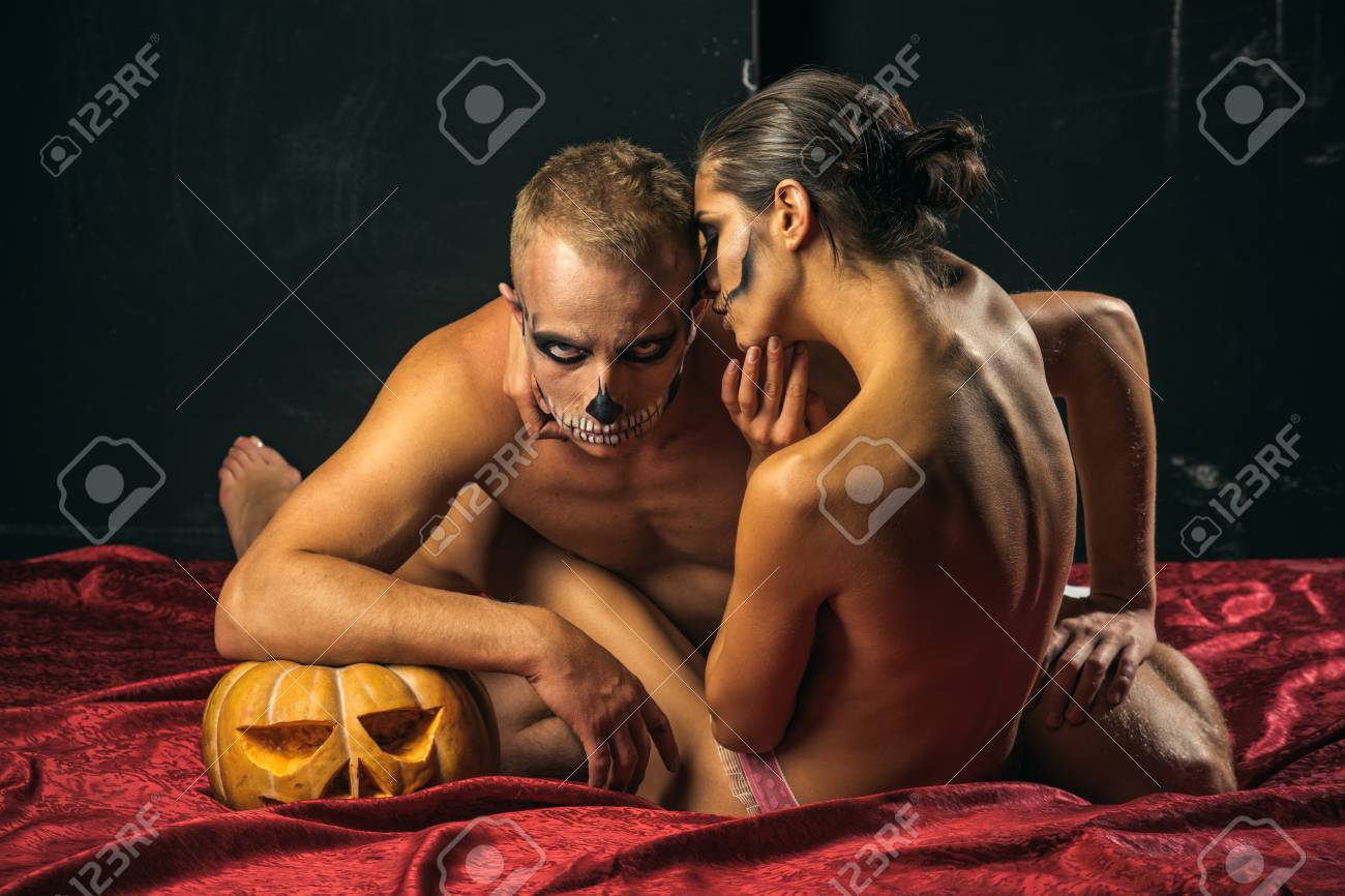 Halloween Couple With Makeup On Red Bedcover. Man And Sexy Woman With Scary  Face Embrace On Bed. Zombie Party And Horror. Halloween Holiday And  Celebration. Couple In Love With Naked Body At