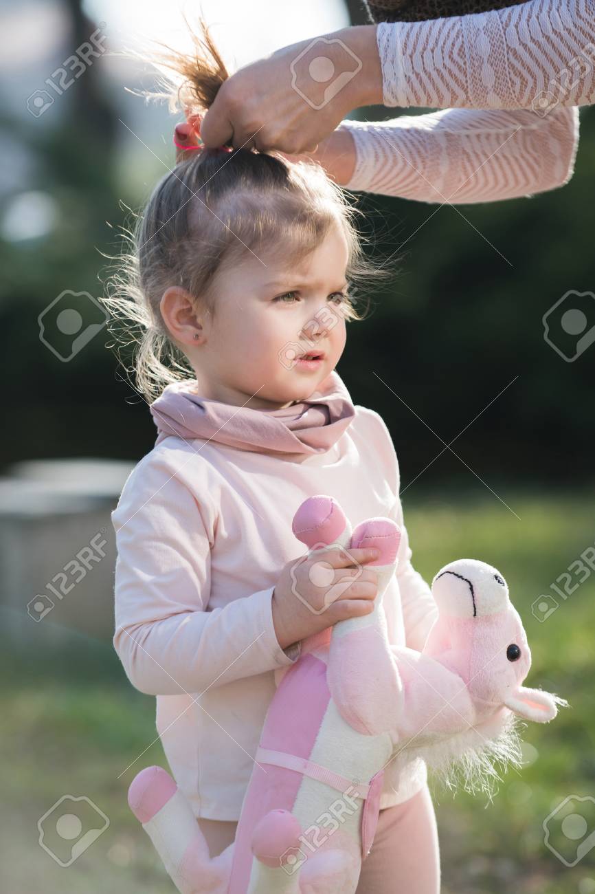 Girl With Toy Horse Get Hair Ponytail Done By Female Hands On