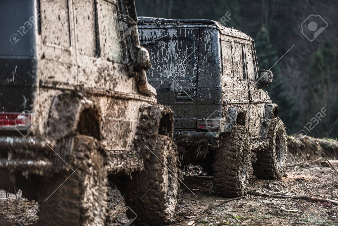 진흙으로 덮인 SUV는 다른 것 뒤에 서 있습니다. 어두운 숲 배경에 더러운 오프로드 자동차입니다. 국가로에서 경주 후 크로스 오버  다시보기. 익스트림 엔터테인먼트 개념. 로열티 무료 사진, 그림, 이미지 그리고 스톡포토그래피. Image 97989297