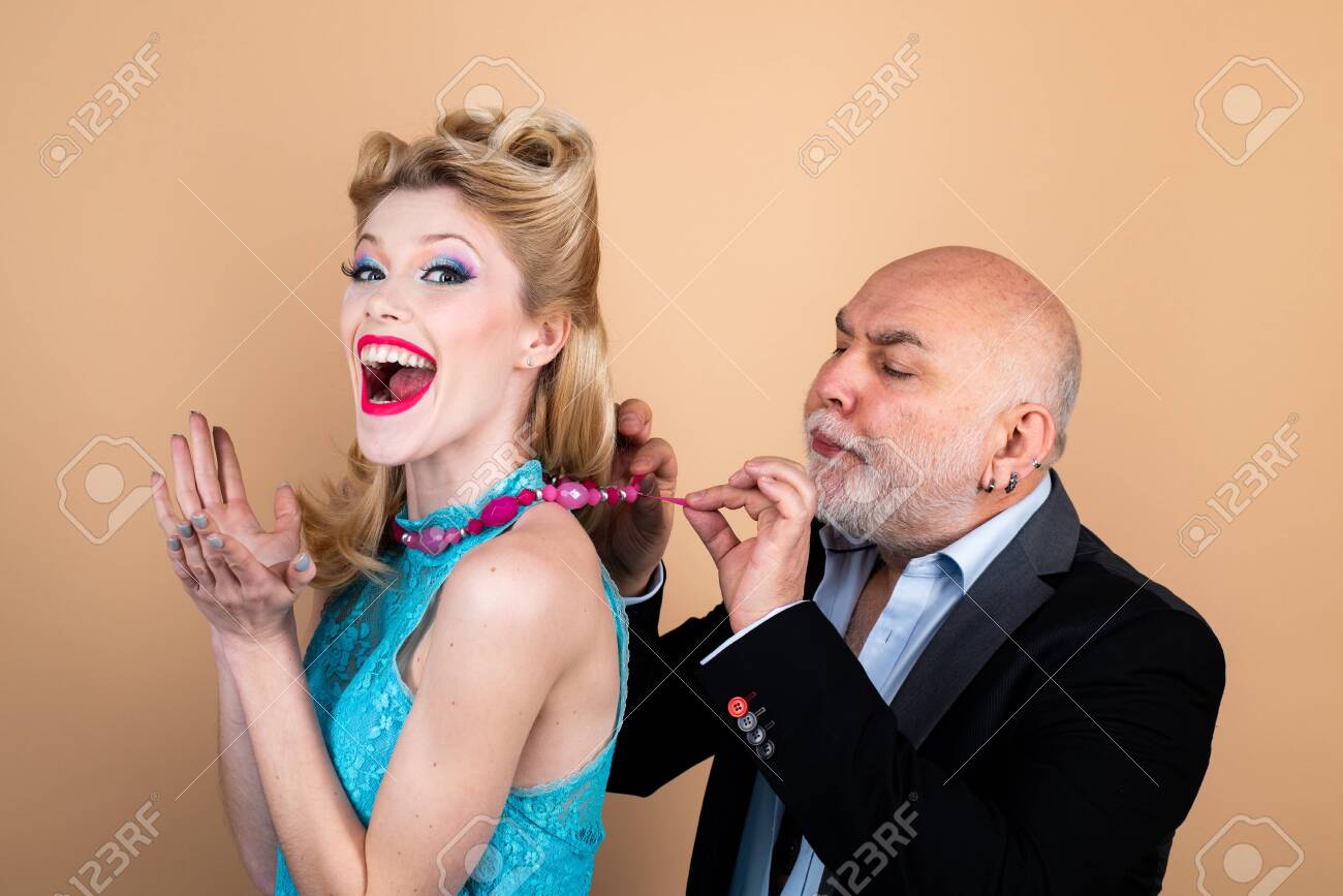 Happy blonde woman with luxury hairstyle and makeup smile while her sugar daddy wears a decoration on her neck. Rich elder man with grey hair. Blonde woman eye wink at camera. - 134343975 Happy blonde woman with luxury hairstyle and makeup smile while her sugar daddy wears a decoration on her neck. Rich elder man with grey hair. Blonde woman eye wink at camera. - 134343975