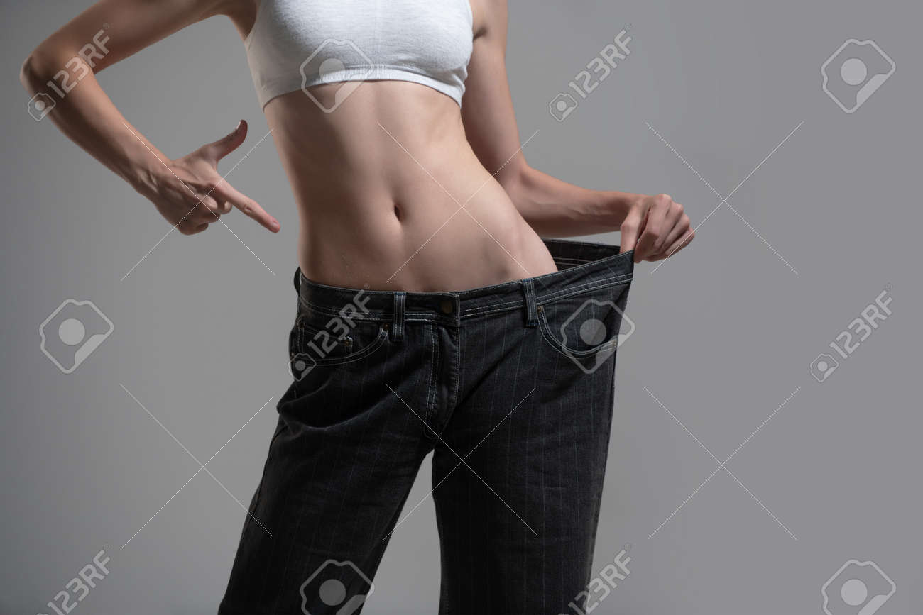 대형 청바지와 다이어트 개념입니다. 너무 큰 청바지에 마른 여자. 성공적인 체중 감량의 개념. 회색 배경에 큰 바지를 입은 얇은 소녀.  로열티 무료 사진, 그림, 이미지 그리고 스톡포토그래피. Image 185048246
