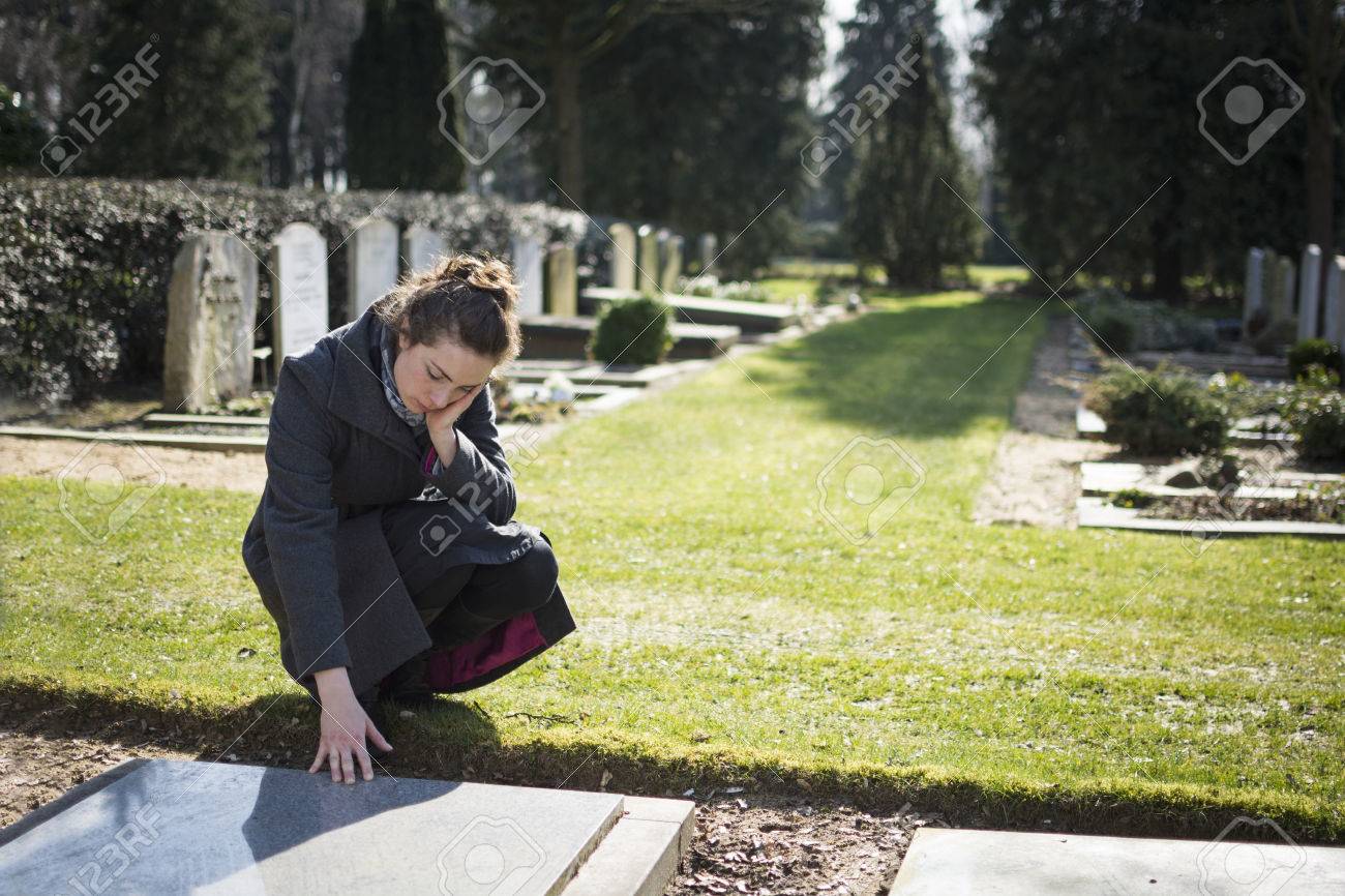 Woman sitting at gravestone on graveyard - 26559182 Woman sitting at gravestone on graveyard - 26559182