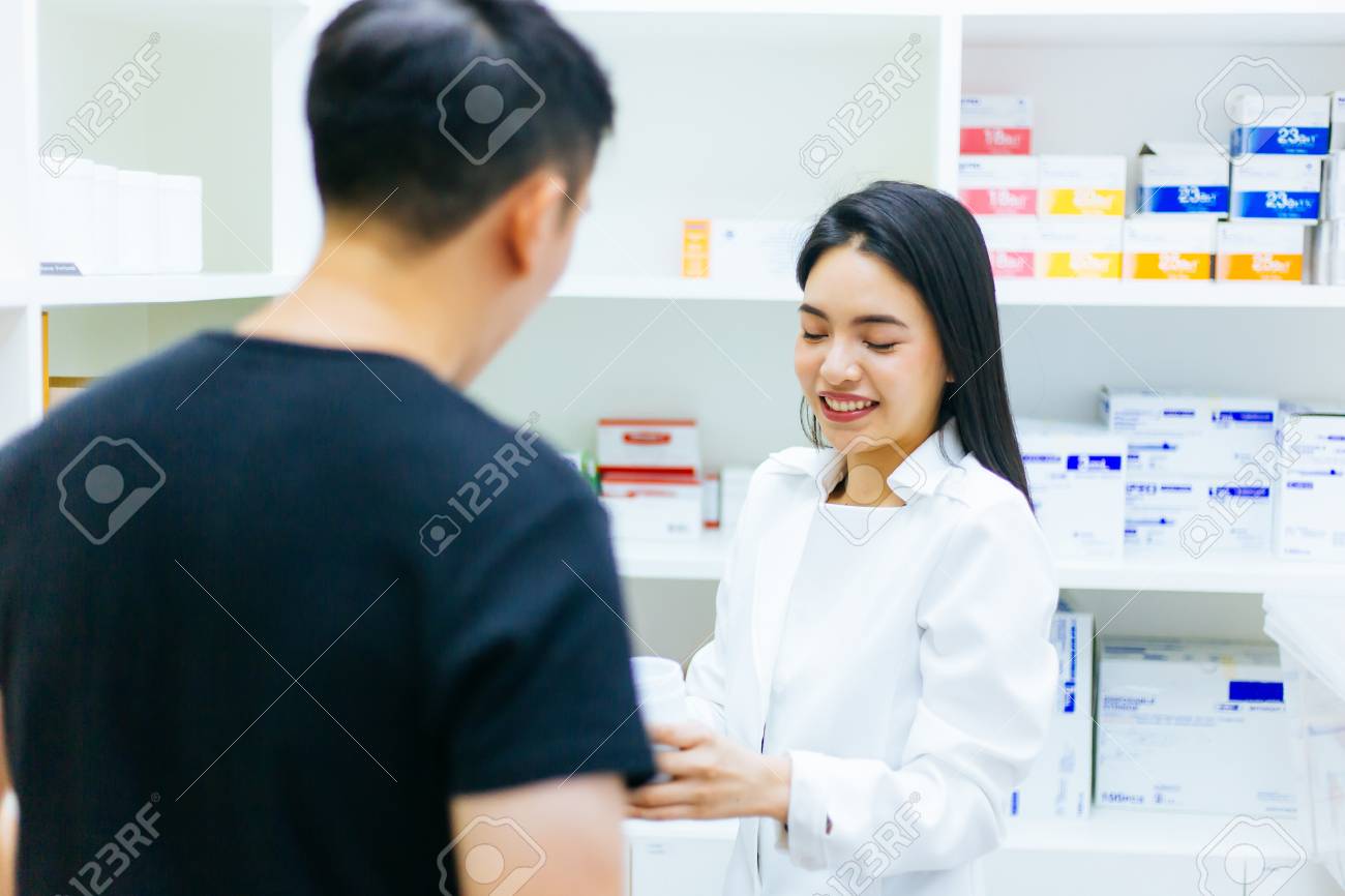 Asian female pharmacist doctor in professional gown explaining and giving advice with male client in drugstore shop - 105455382 Asian female pharmacist doctor in professional gown explaining and giving advice with male client in drugstore shop - 105455382