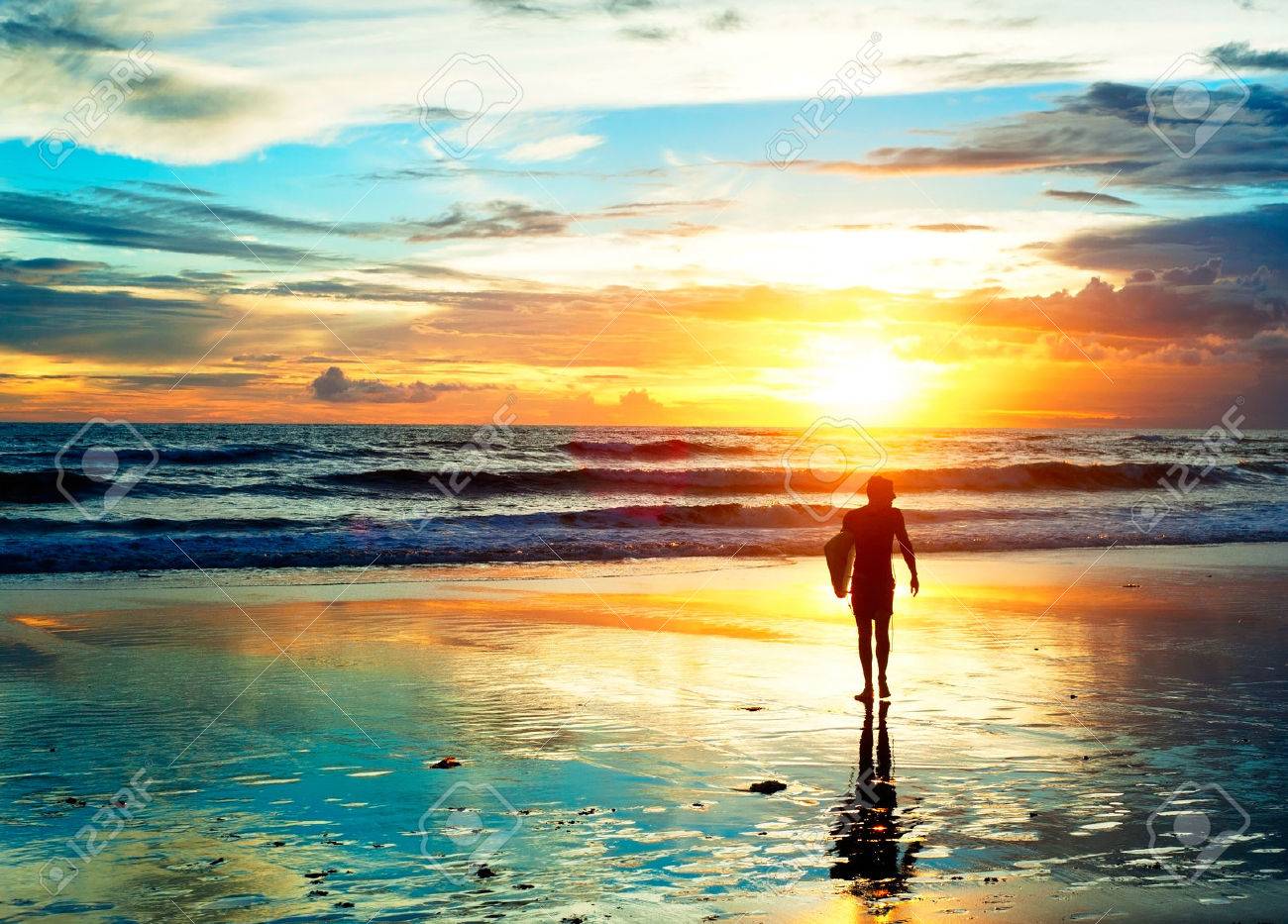 Surfer walking on the beach in sunset light. Bali island, Indonesia - 33067098 Surfer walking on the beach in sunset light. Bali island, Indonesia - 33067098