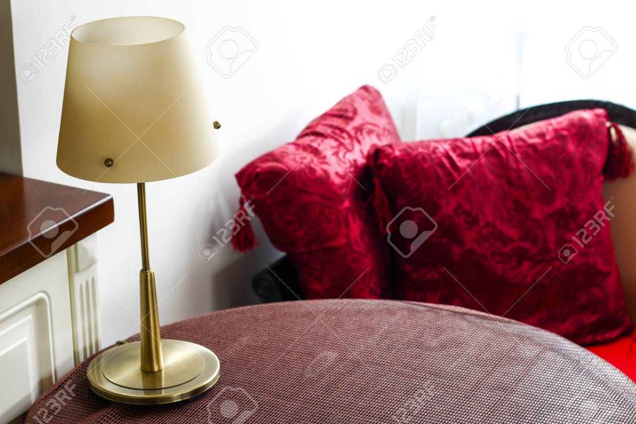 Habitación con una mesa con mantel marrón, lámpara y cojines rojos Habitación con una mesa con mantel marrón, lámpara y cojines rojos