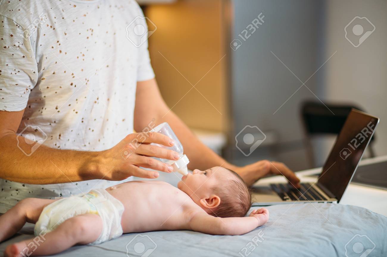 dad trying to work while standing with his newborn babe in home office interior - 92314699 dad trying to work while standing with his newborn babe in home office interior - 92314699