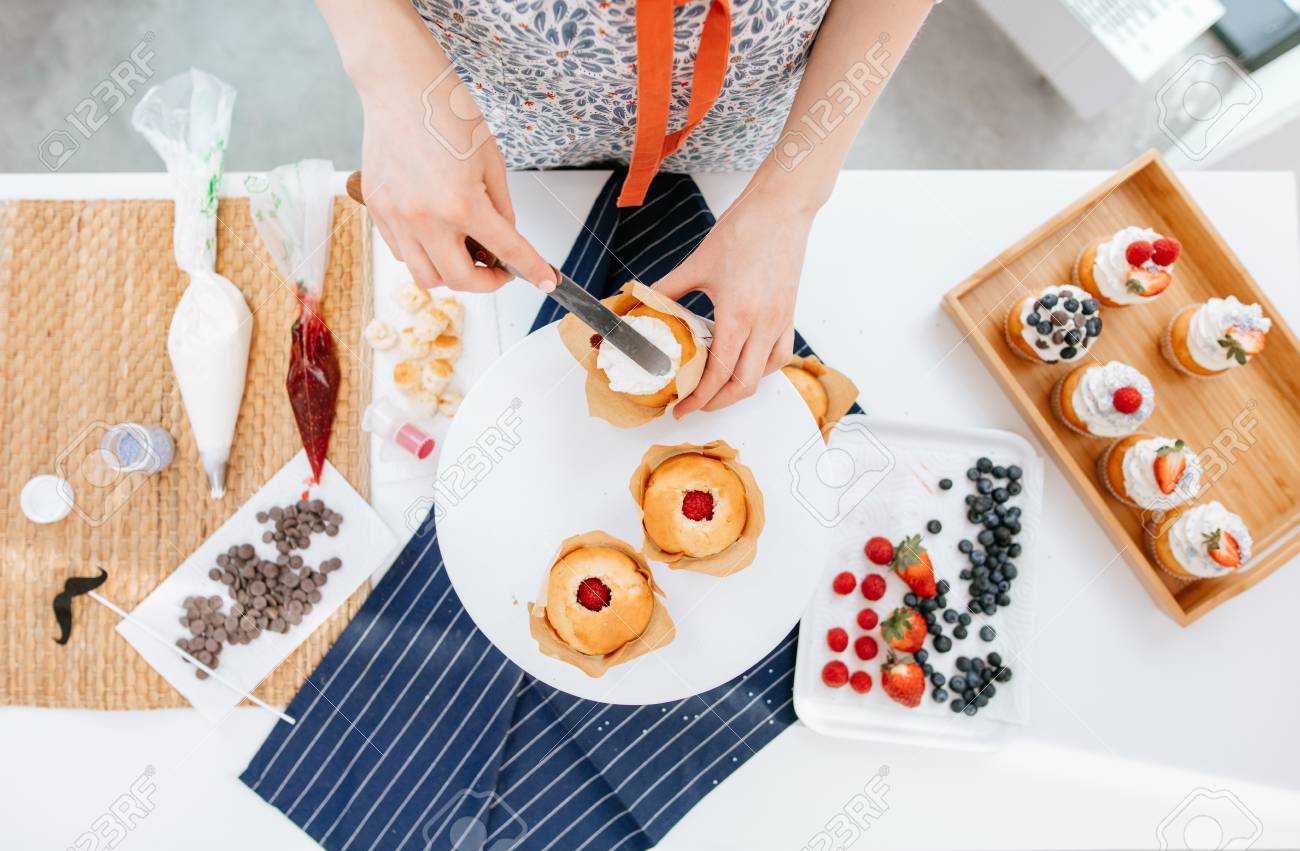 Confectioner woman topping a cupcake with cream using a knife. - 99141679 Confectioner woman topping a cupcake with cream using a knife. - 99141679
