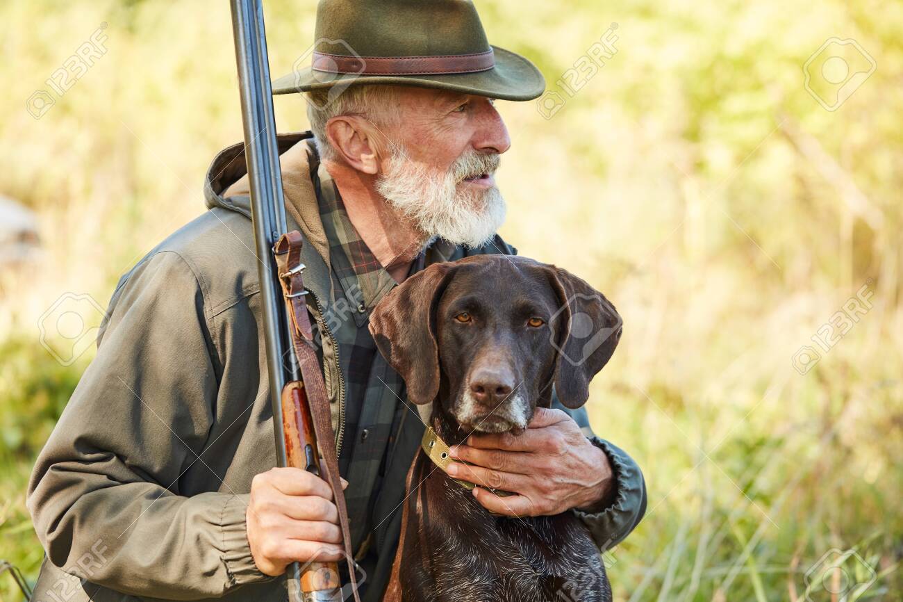 Caucasian mature man with gun and dog sit searching prey. Bearded man in hunting clothes. Autumn - 133175309 Caucasian mature man with gun and dog sit searching prey. Bearded man in hunting clothes. Autumn - 133175309