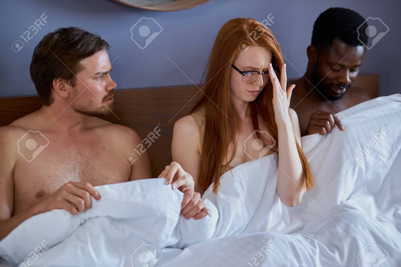 Interracial Couple Having Complicated Affair And Love Triangle In Bedroom, Redhead Woman At A Loss Stock Photo, Picture and Royalty Free Image