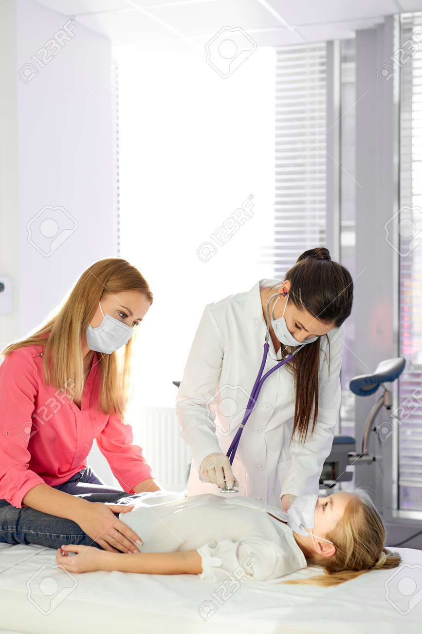 female doctor checks heartbeat and lungs using stethoscope during coronavirus epidemic, mother supports patient daughter, in medical masks - 169036677 female doctor checks heartbeat and lungs using stethoscope during coronavirus epidemic, mother supports patient daughter, in medical masks - 169036677