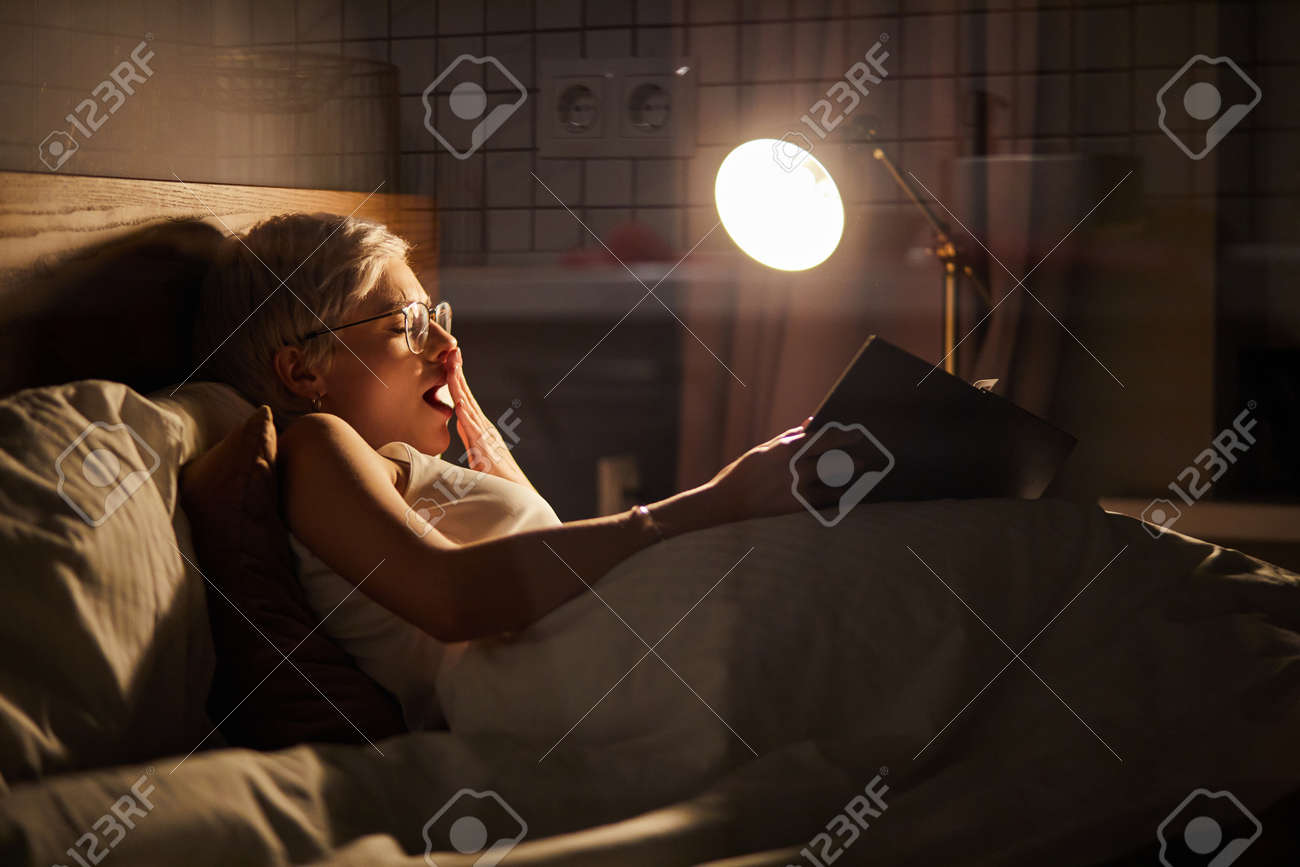 Tired Bored Woman Reading Novel Before Going to Bed. Bored Female Holding Book And Yawning, Trying To Get Sleepy Fighting Insomnia - 169368808 Tired Bored Woman Reading Novel Before Going to Bed. Bored Female Holding Book And Yawning, Trying To Get Sleepy Fighting Insomnia - 169368808