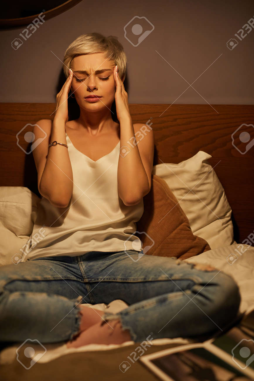 Portrait Of Young Lady Suffering From Headache, Sitting On Bed At Home Alone, Woman Touching Head, Bored And Exhausted, Need Some Rest, Depressed - 169368833 Portrait Of Young Lady Suffering From Headache, Sitting On Bed At Home Alone, Woman Touching Head, Bored And Exhausted, Need Some Rest, Depressed - 169368833