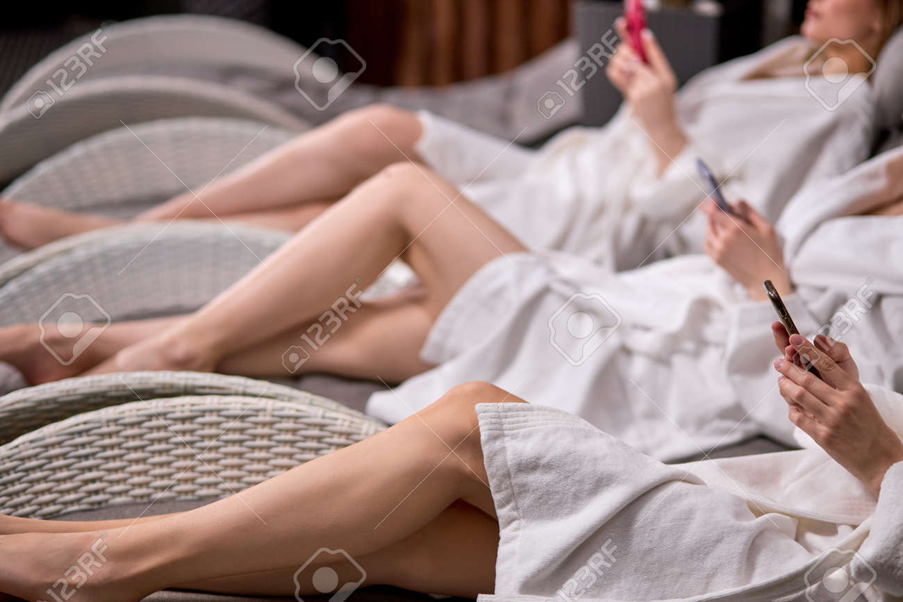 Side view on cropped women with smartphone in spa center, wearing bathrobes, unrecognizable ladies chatting, surfing the Net after beauty procedures - 169368933 Side view on cropped women with smartphone in spa center, wearing bathrobes, unrecognizable ladies chatting, surfing the Net after beauty procedures - 169368933