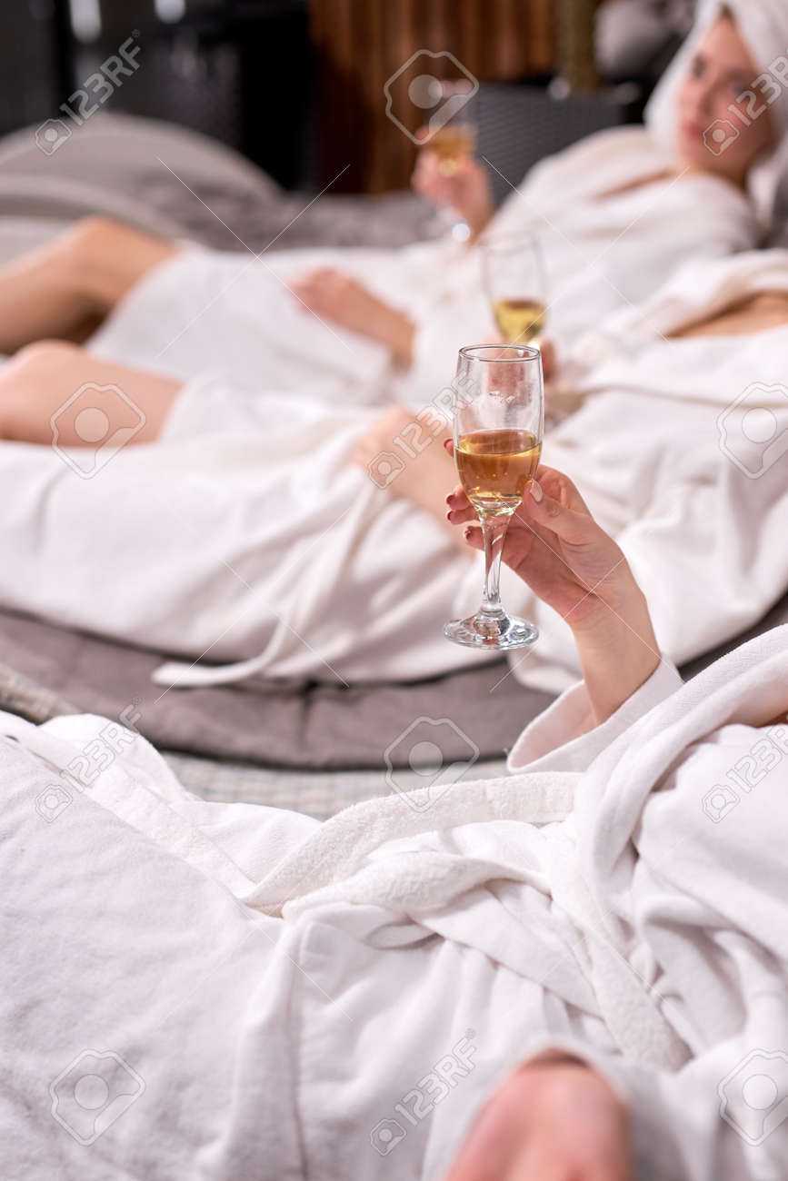 Cropped ladies in bathrobes drinking champagne after spa procedures. Spa hotel vacation concept. Cropped photo of females holding glasses. Focus on hands - 169368949 Cropped ladies in bathrobes drinking champagne after spa procedures. Spa hotel vacation concept. Cropped photo of females holding glasses. Focus on hands - 169368949