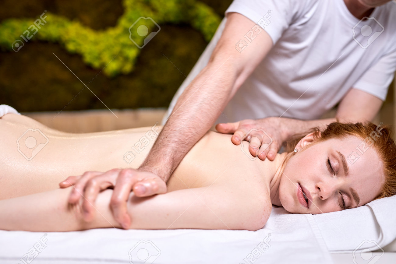 Unrecognizable male therapist massaging redhead attractive woman lying relaxed with eyes closed on stomach, side view. Professional treatment by masseur, in spa center - 169368960 Unrecognizable male therapist massaging redhead attractive woman lying relaxed with eyes closed on stomach, side view. Professional treatment by masseur, in spa center - 169368960