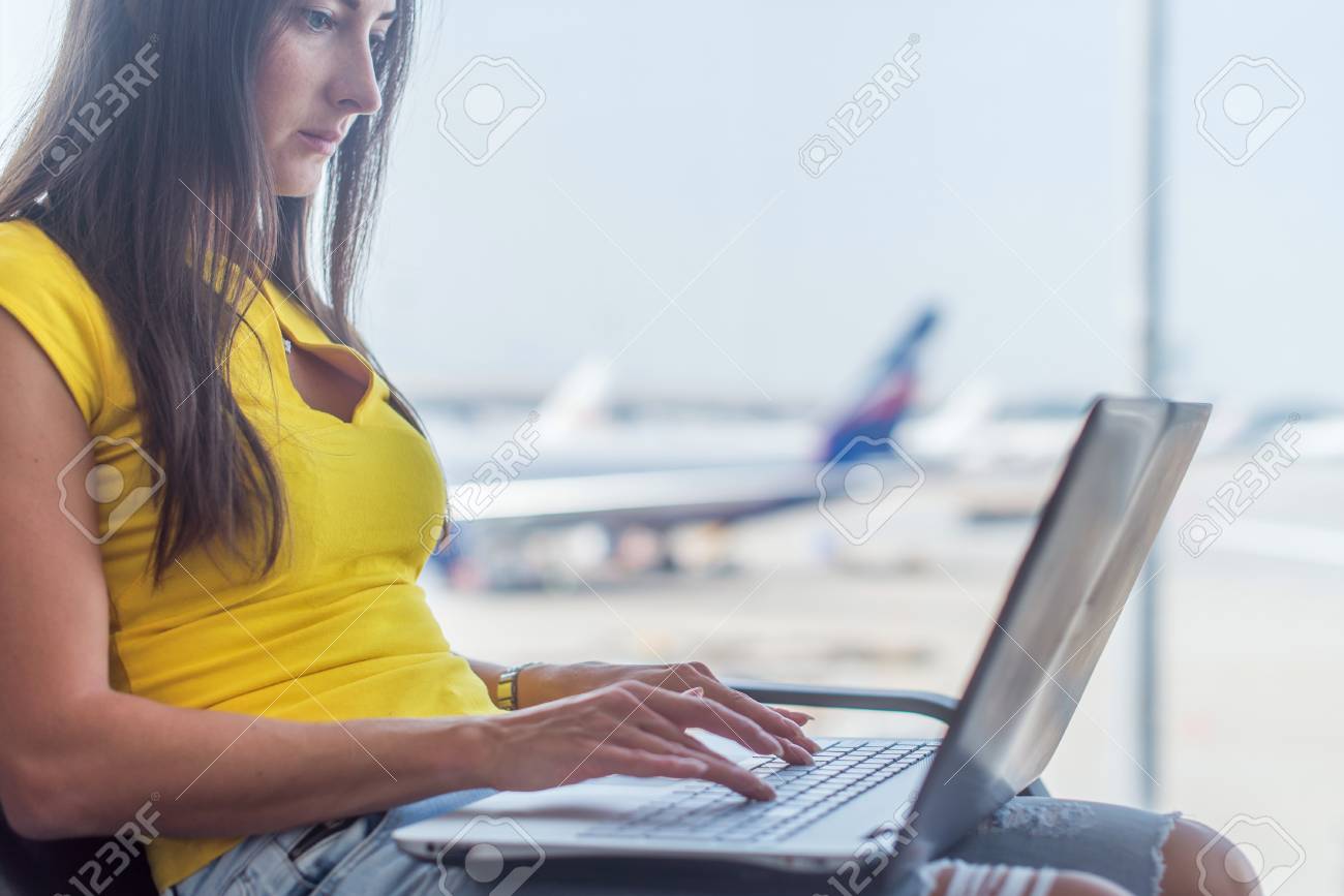 若い女性が空港に屋内でキーボードを入力する膝の上のラップトップを保持 の写真素材 画像素材 Image