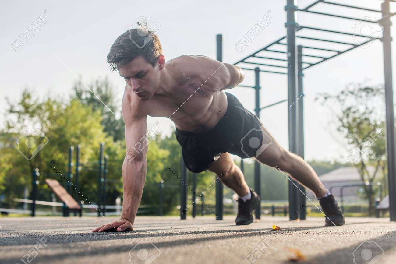 Athlete young man doing one-arm push-up exercise working out his upper body muscles outside in summer. - 84119624 Athlete young man doing one-arm push-up exercise working out his upper body muscles outside in summer. - 84119624