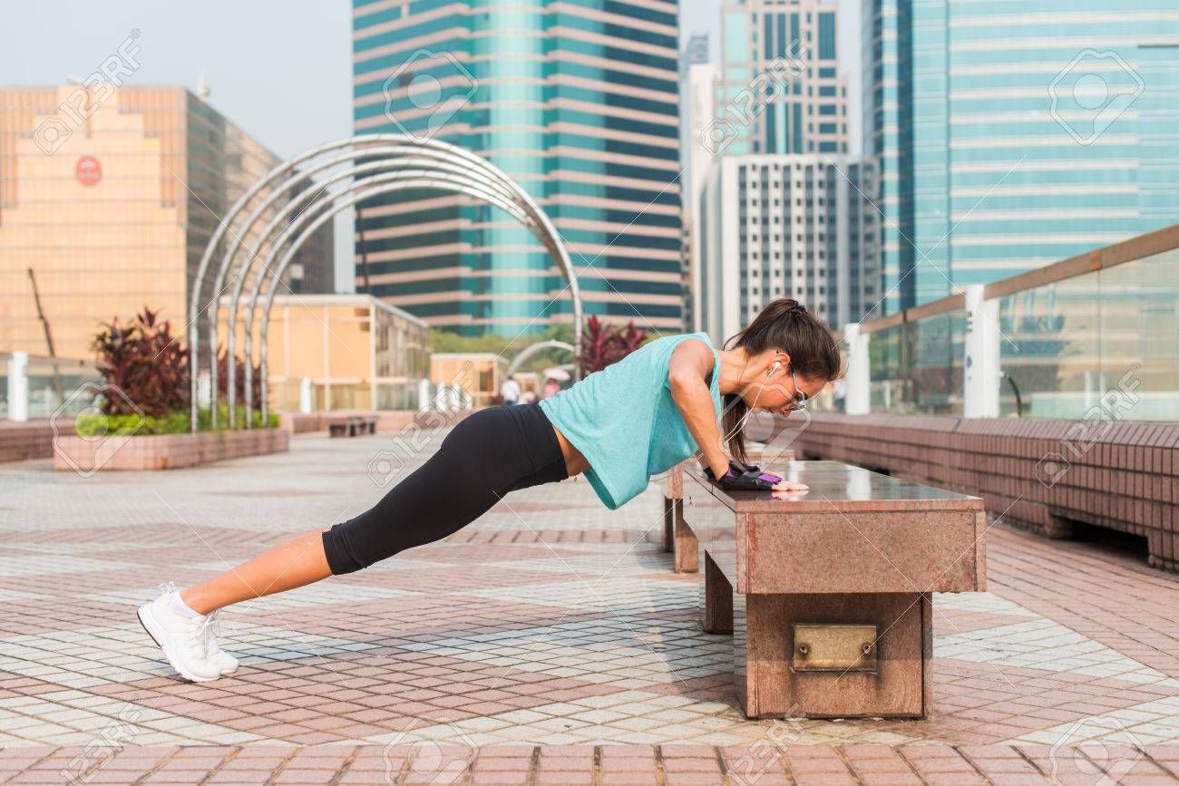 Fitness woman doing feet elevated push-ups on a bench in the city. Sporty girl exercising outdoors - 84049214 Fitness woman doing feet elevated push-ups on a bench in the city. Sporty girl exercising outdoors - 84049214
