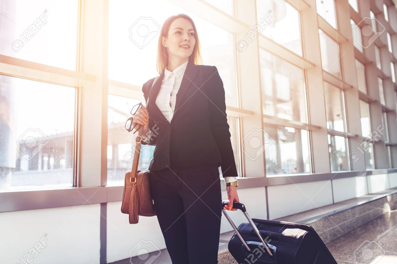 Pretty smiling female flight attendant carrying baggage going to airplane in the airport - 90059352 Pretty smiling female flight attendant carrying baggage going to airplane in the airport - 90059352