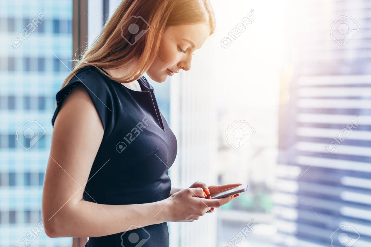 Pretty smilingwoman using smartphone standing in office - 91427289 Pretty smilingwoman using smartphone standing in office - 91427289