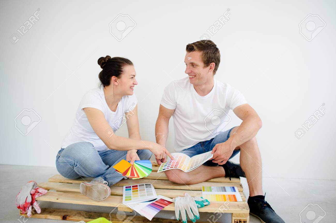 Couple Enthousiaste Choisit La Couleur De La Peinture Pour La Reparation Dans La Chambre Ils Sont Assis Sur Un Plancher Et Se Regardent Dans Leurs Mains Des Exemples De Couleur Bon Mur