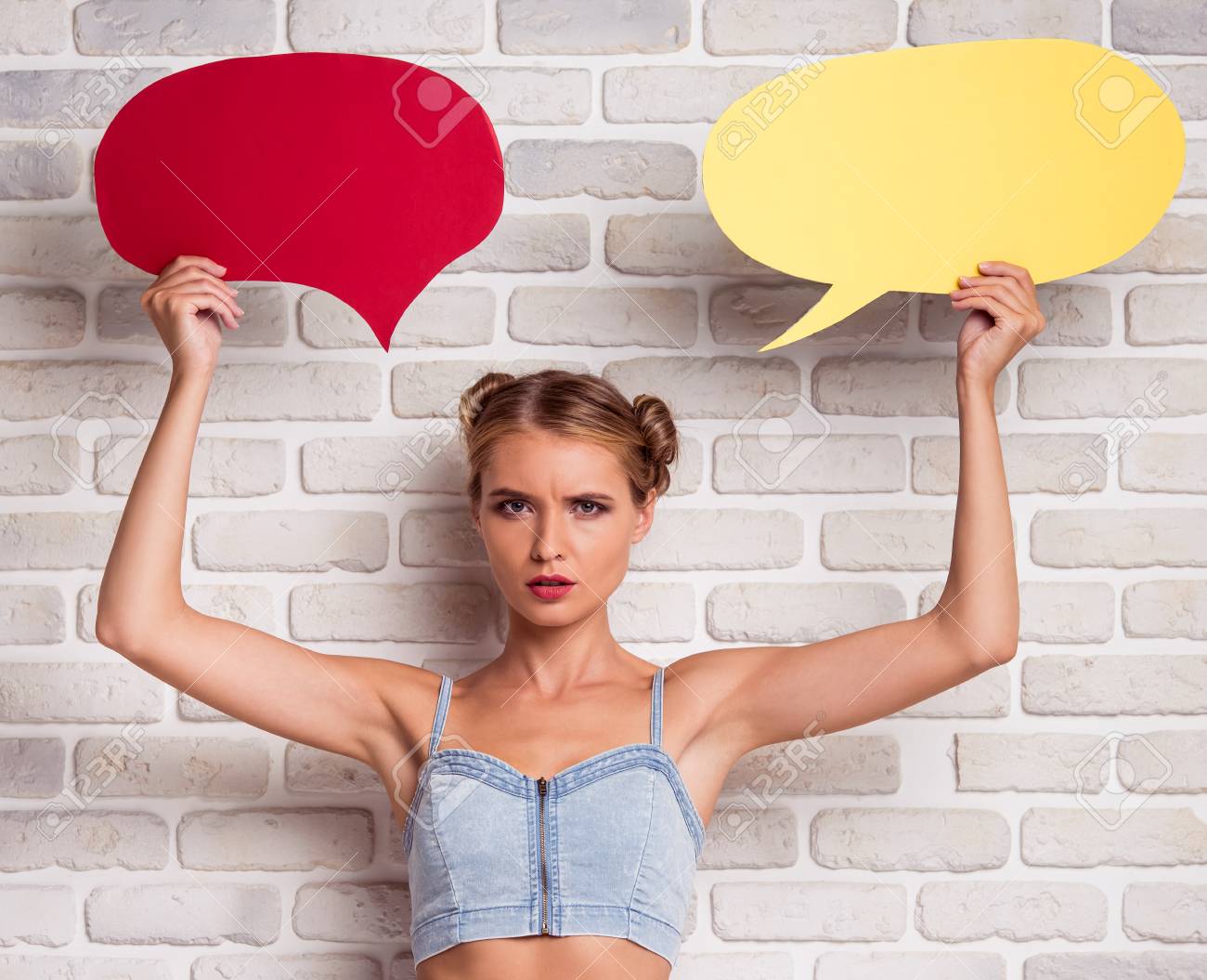 Beautiful Stylish Girl In Jeans Top And White Shorts Is Holding Speech Bubbles Looking At Camera And Frowning On White Brick Wall Background Stock Photo Picture And Royalty Free Image Image