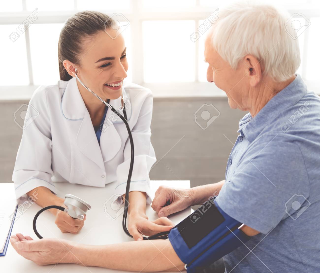 Beautiful Female Doctor In White Medical Coat Is Testing Patient's Blood Pressure And Smiling While Sitting In Office Stock Photo, Picture And Royalty Free Image. Image 65187921.