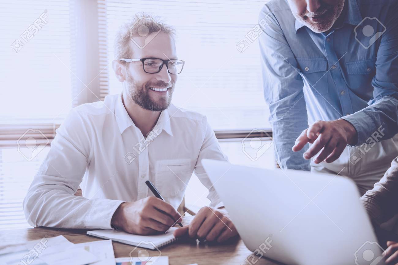Business people are using a laptop, discussing affairs and smiling while working in office - 100725931 Business people are using a laptop, discussing affairs and smiling while working in office - 100725931