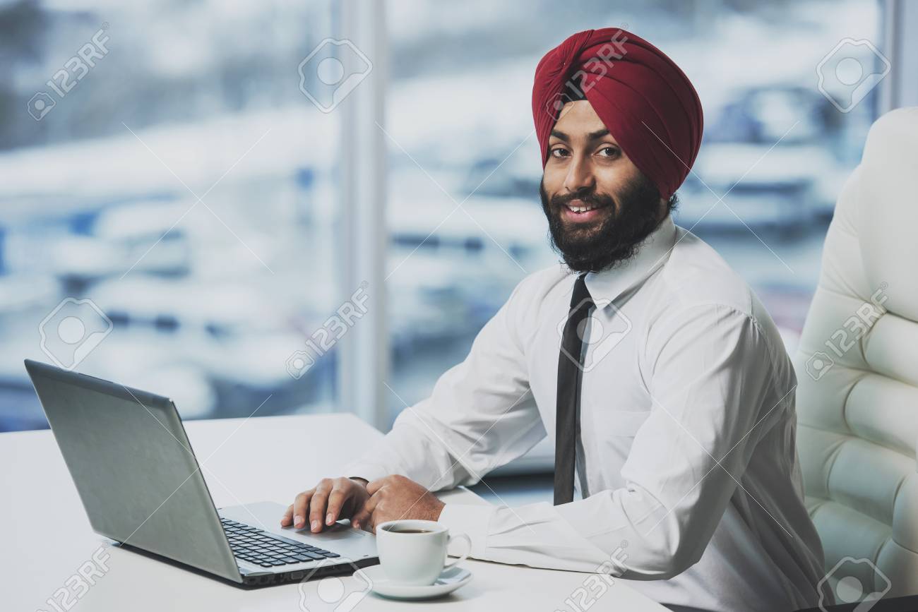 Young indian bearded businessman working behind laptop in modern office. Business people. - 102947120 Young indian bearded businessman working behind laptop in modern office. Business people. - 102947120