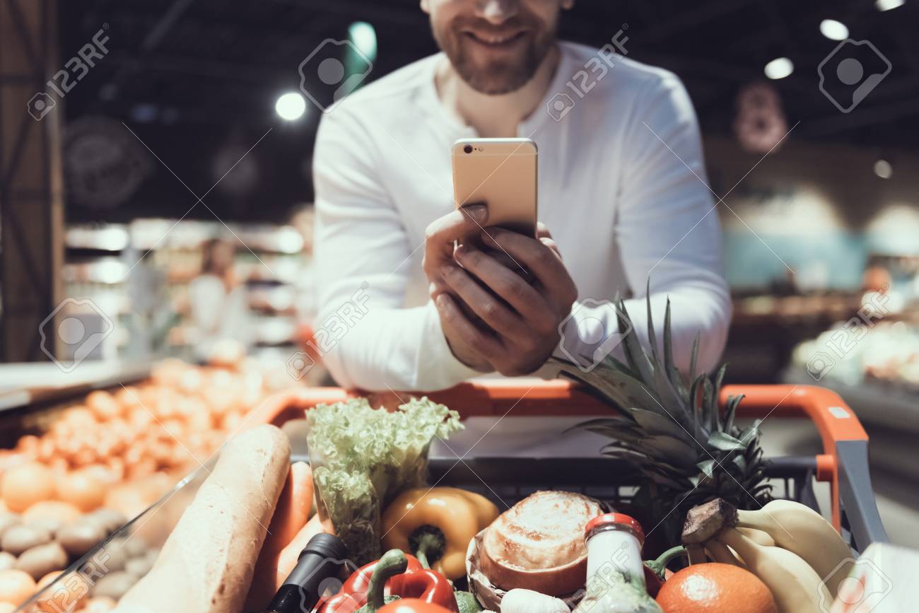 Close up. Man Using Cell Phone near Shopping Trolley. Father with Shopping Trolley. Shopping Cart with Food. Consumerism Concept. Man in Shirt. Shopping in Supermarket. Digital Device. - 105135357 Close up. Man Using Cell Phone near Shopping Trolley. Father with Shopping Trolley. Shopping Cart with Food. Consumerism Concept. Man in Shirt. Shopping in Supermarket. Digital Device. - 105135357