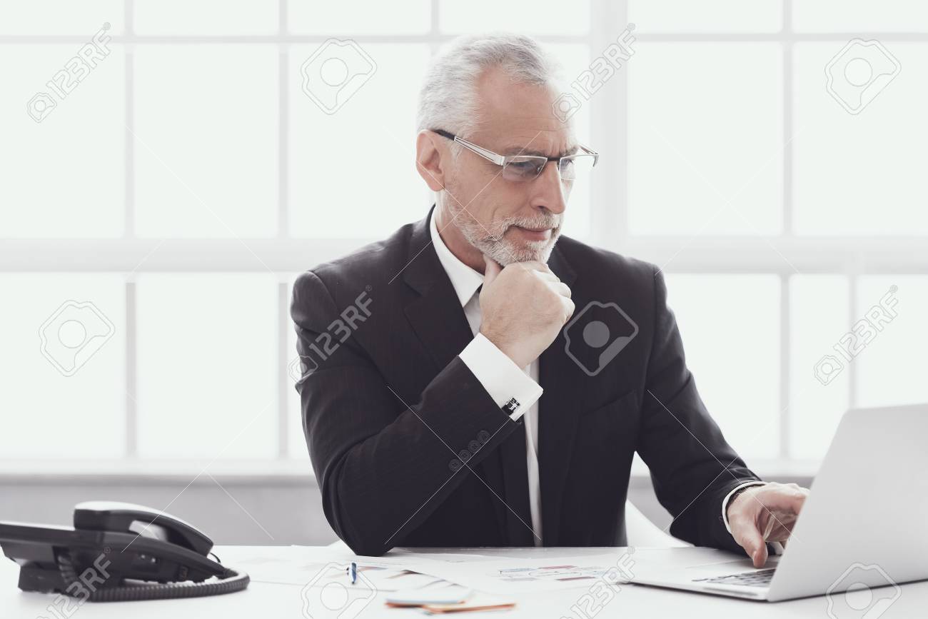 Adult Businessman Working on Laptop in Office. Professional Mature Bearded Worker Sitting at Desk and Working on Computer. Successful Businessman wearing Suit at Work. Corporate Lifestyle Concept - 107272205 Adult Businessman Working on Laptop in Office. Professional Mature Bearded Worker Sitting at Desk and Working on Computer. Successful Businessman wearing Suit at Work. Corporate Lifestyle Concept - 107272205