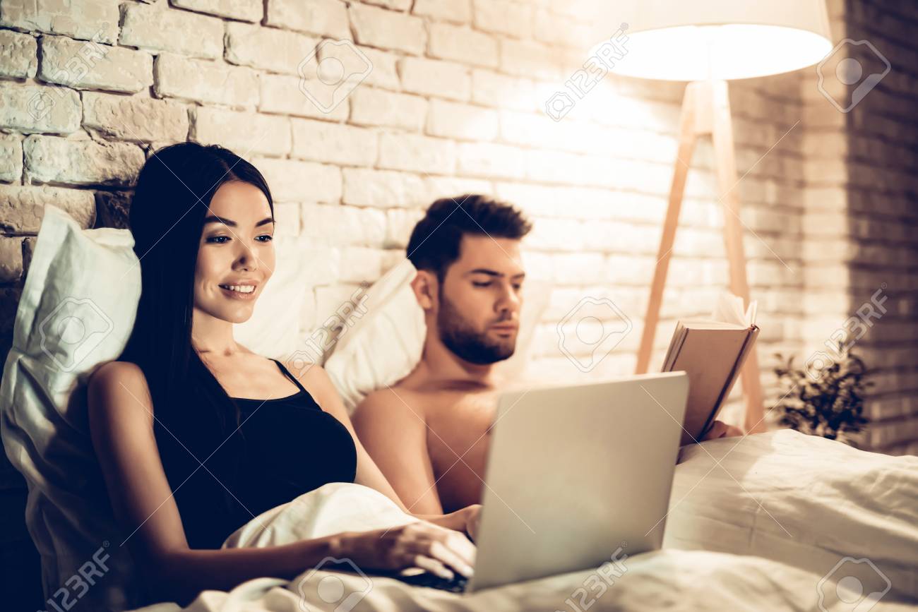 Couple Using Laptop Reading Book Before Sleeping. Young Guy Watching Movie or Browsing Internet. Girl Reading Book at Night. Relationship Concept. Wife and Husband. - 113961727 Couple Using Laptop Reading Book Before Sleeping. Young Guy Watching Movie or Browsing Internet. Girl Reading Book at Night. Relationship Concept. Wife and Husband. - 113961727