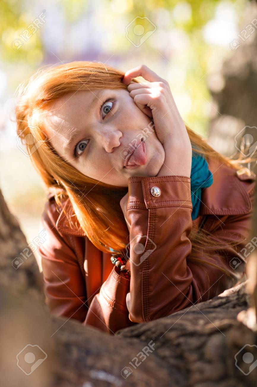 変な顔を作ると舌の木の近くの公園でポーズを示すかなり面白い赤毛の女の子 の写真素材 画像素材 Image