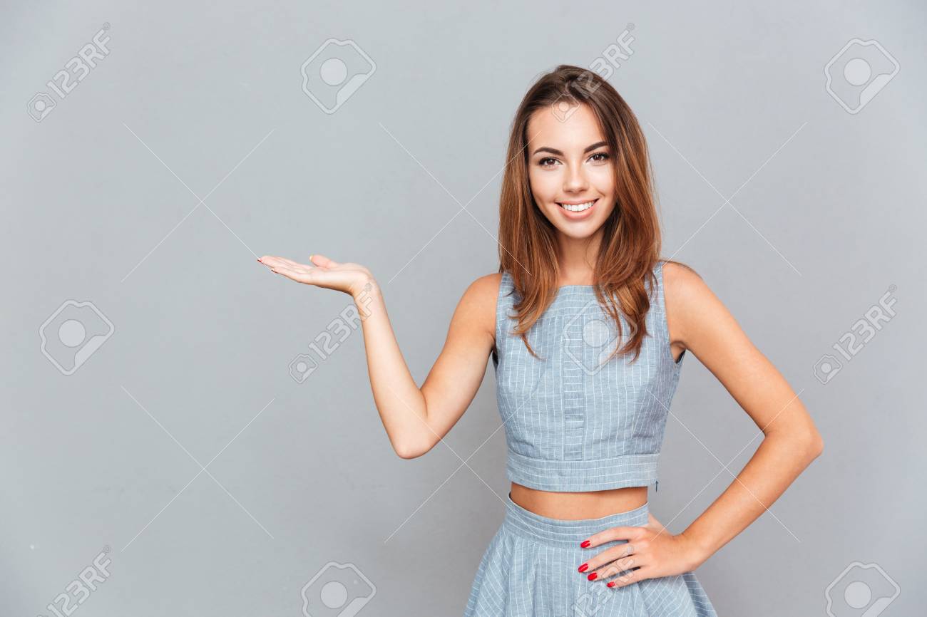Happy beautiful young woman holding copyspace on palm over grey background - 63562347 Happy beautiful young woman holding copyspace on palm over grey background - 63562347
