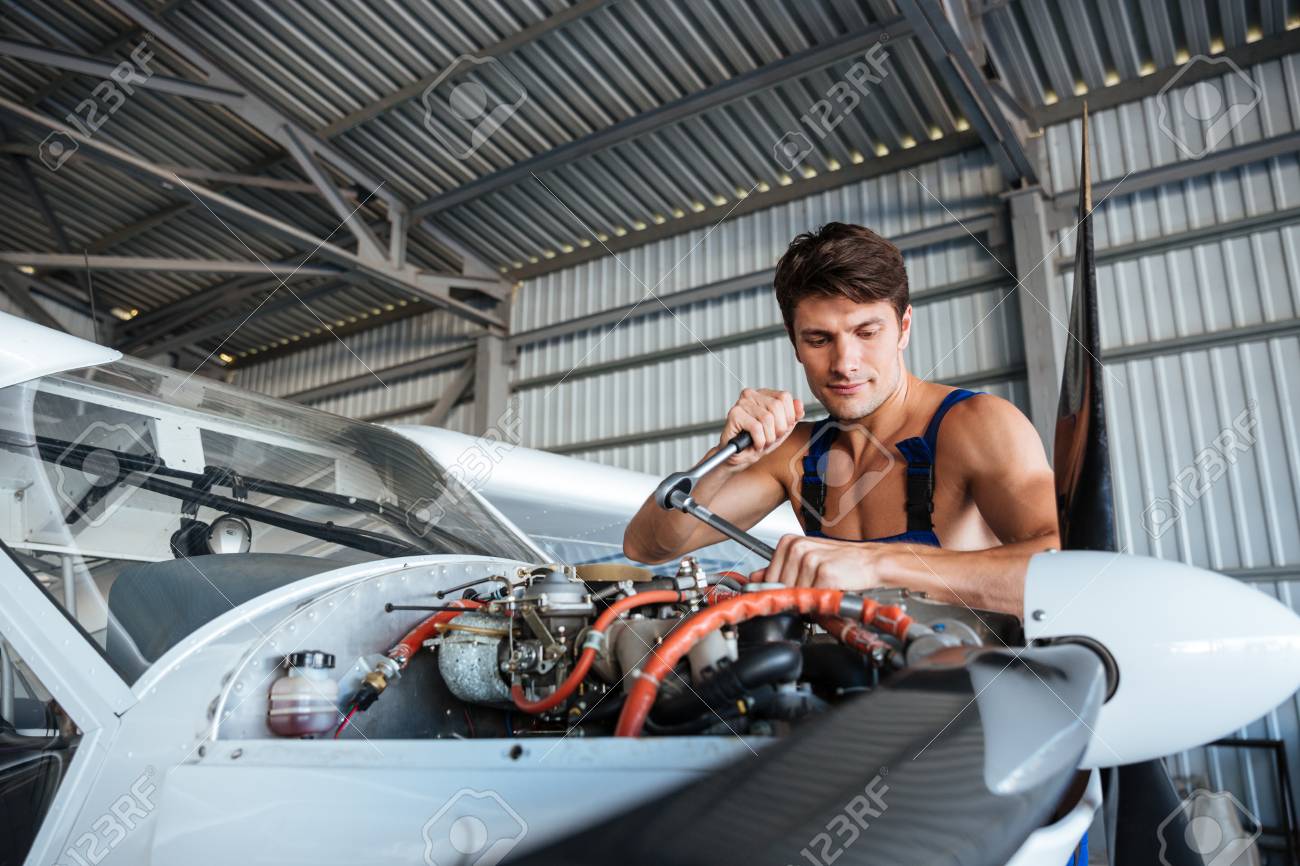 Serious Young Aircraft Mechanic Standing And Fixing Small Airplane