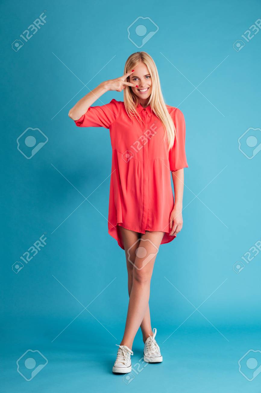 Retrato De Corpo Inteiro De Uma Mulher Loira Sorridente Em Pe De Vestido Vermelho E Mostrando Sinal De Vitoria Isolado Em Um Fundo Azul Fotos Retratos Imagenes Y Fotografia De Archivo Libres