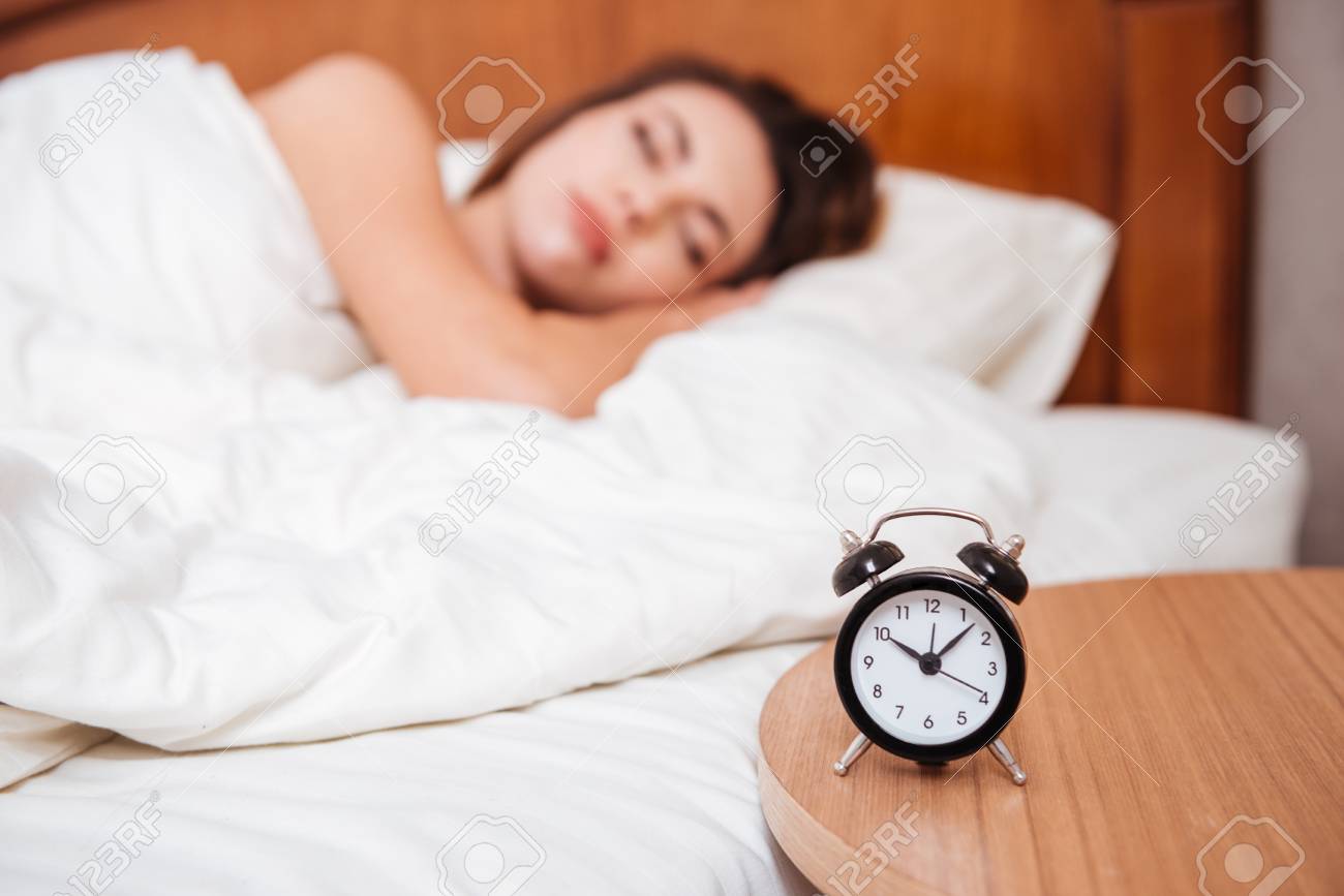 young woman sleeping in bed in her bedroom focus on alarm clock