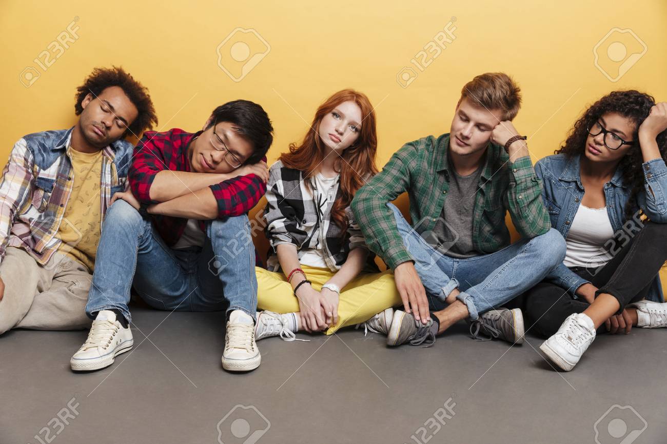 group of tired young people sitting and sleeping over yellow stock