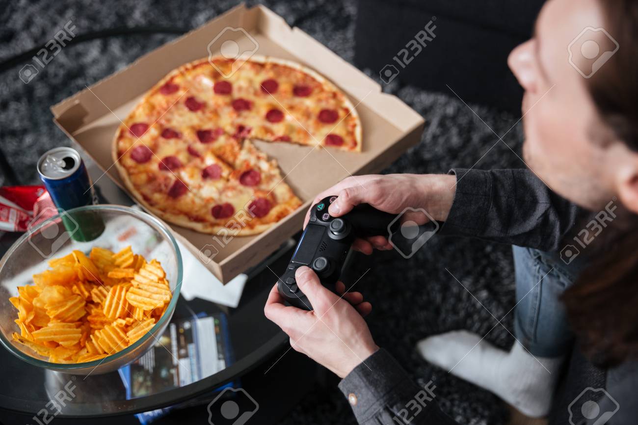 切り取られた写真の若いゲーマーに自宅室内で座って男し ピザ ポテトチップスのジョイスティックとゲームをプレイします の写真素材 画像素材 Image