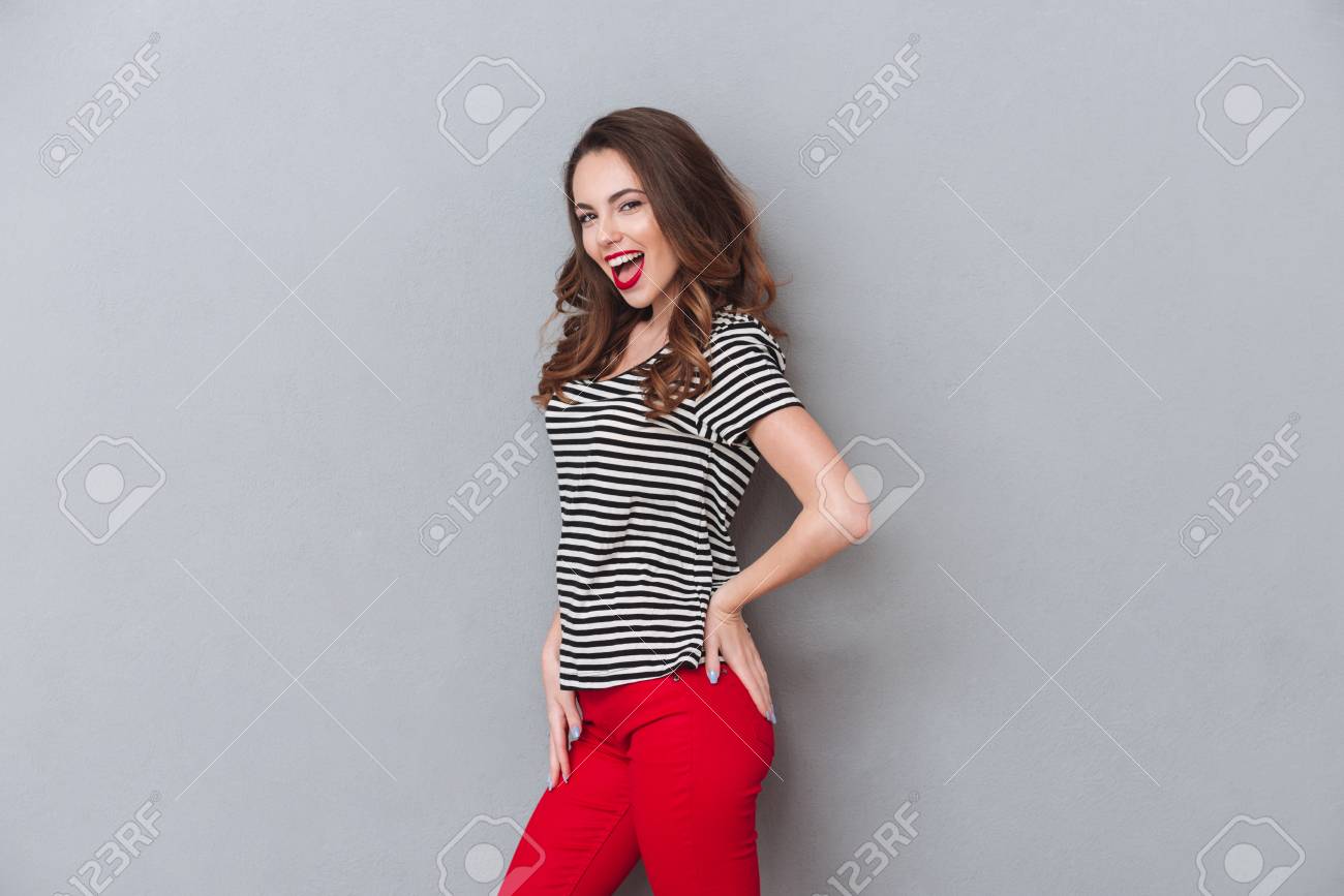横向きポーズのきれいな女性を笑顔と灰色の背景の上のカメラを見て の写真素材 画像素材 Image