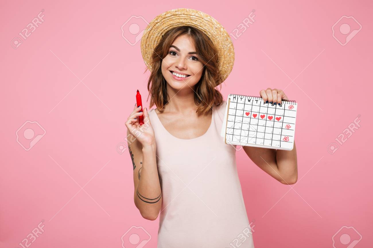 Portrait of a young smiling girl in summer hat checking her periods with a calendar and a felt-tip pen isolated over pink background - 90184107 Portrait of a young smiling girl in summer hat checking her periods with a calendar and a felt-tip pen isolated over pink background - 90184107
