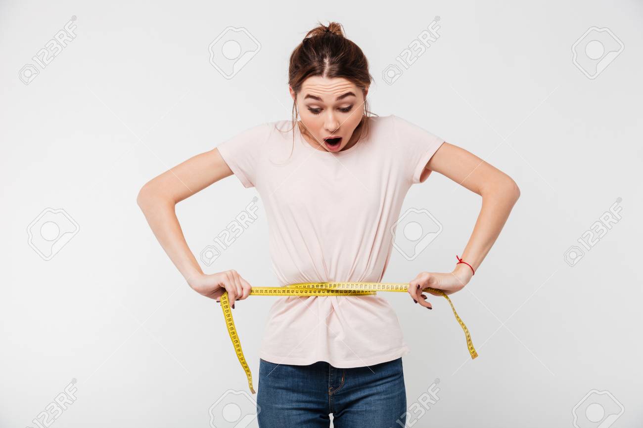 Portrait of a slim astonished woman holding measuring tape around her waist isolated over white background - 91792302 Portrait of a slim astonished woman holding measuring tape around her waist isolated over white background - 91792302